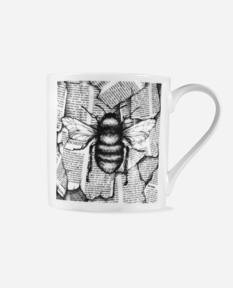 Manchester bee mug in white bone china showing front view of black bee illustration on newsprint background