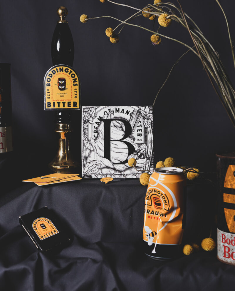 White ceramic tile with black illustrated B design featuring Boddington's Brewery text with hops and barley illustrations on yellow surface