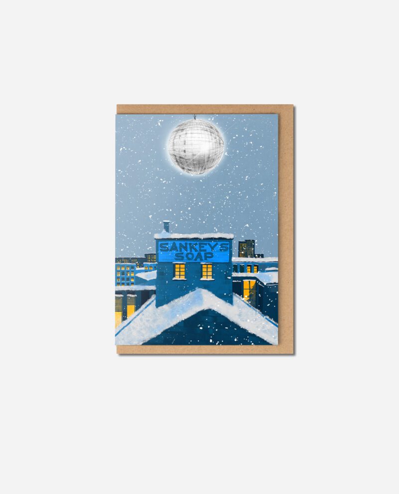 Sankey's Soap Christmas card flat lay showing blue Beehive Mill with snow, disco ball and yellow windows by The Sculpts