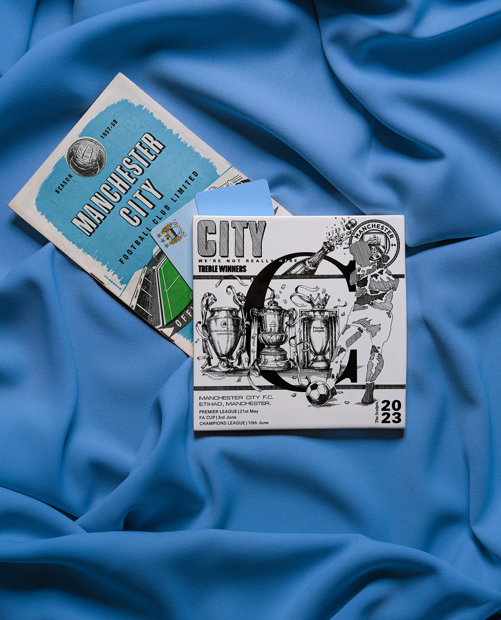 Man City Treble Tile with vintage 1960s programme and light blue Citizen Cards on sky blue fabric background