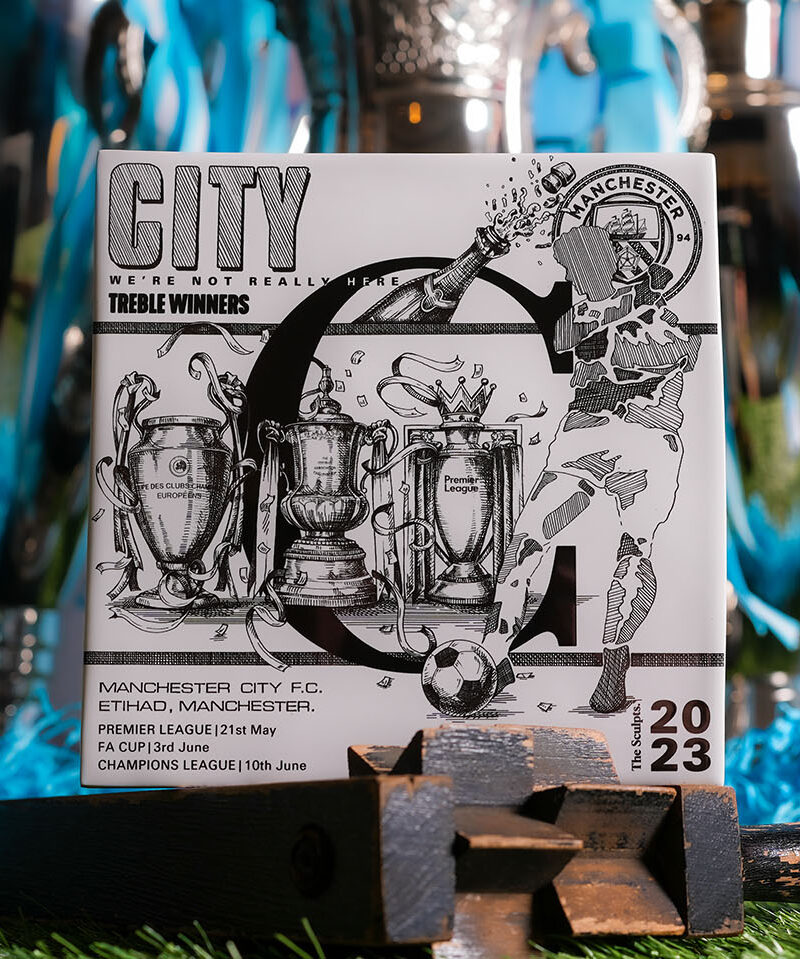 Manchester City Treble tile in black and white showing three trophies surrounded by sky blue ribbons and shredded paper