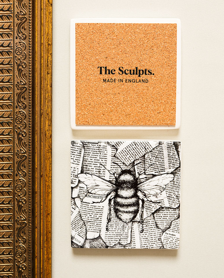 Newspaper Bee coaster with illustrated bee design, shown front and back, styled beside an ornate gold frame on a soft cream background.