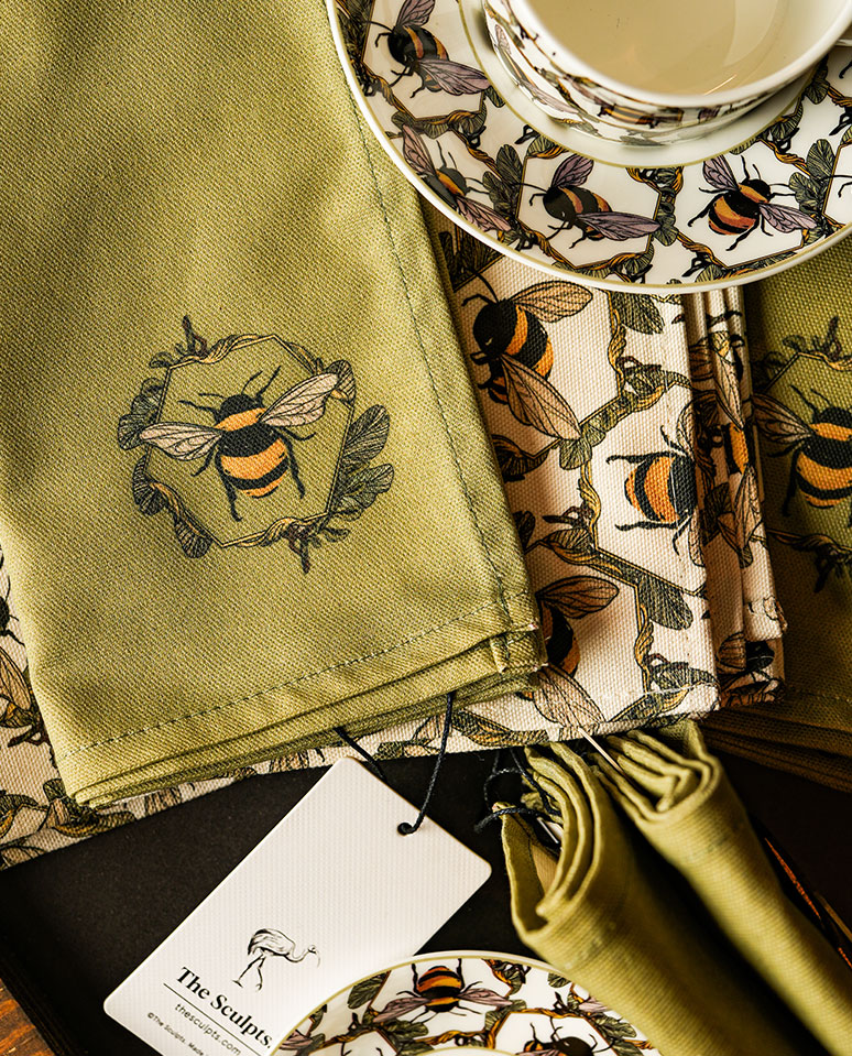 Honeycomb Bee napkins and tea towels styled together with matching illustrated tableware, featuring green and cream textiles with hand-drawn bee motifs in a warm, natural setting.