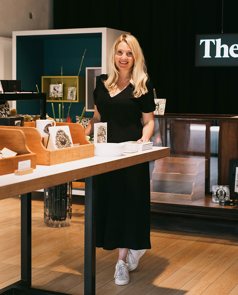 Woman standing at wooden display counter with handmade ceramic mugs and design samples